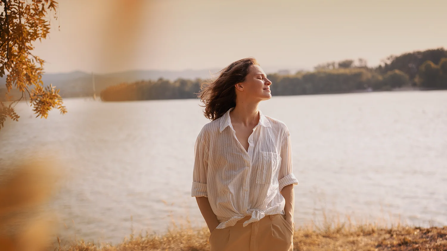 A relaxed woman smiles near a lake