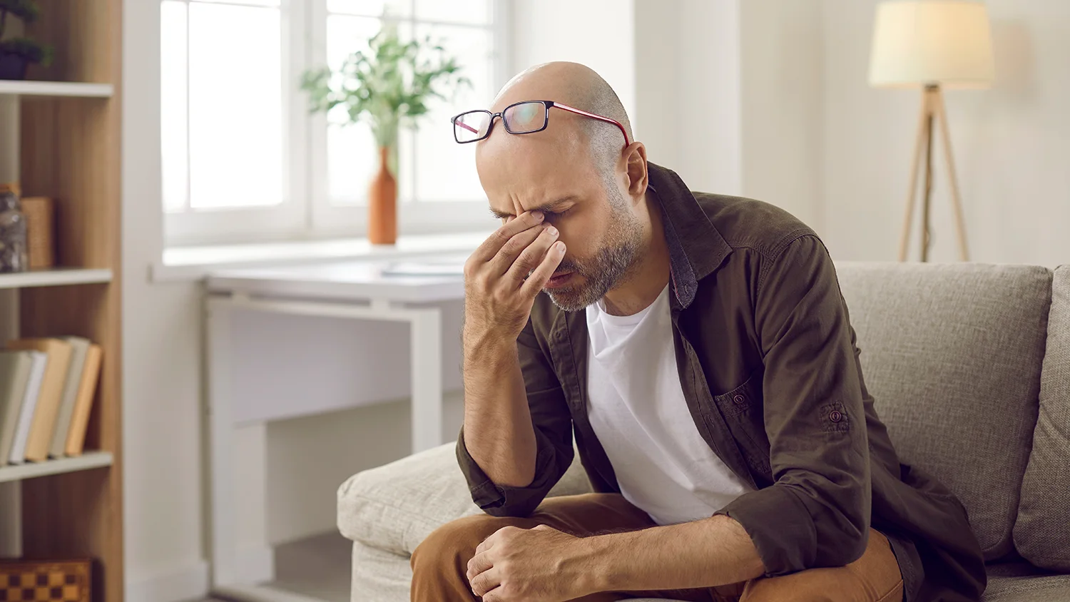 an exhausted man holds his head while sitting on a couch