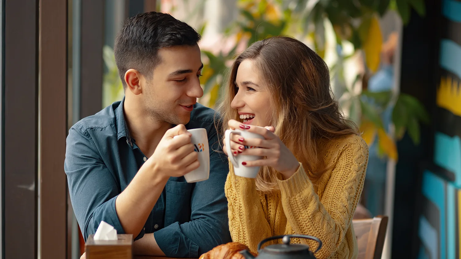 a happy couple smiles while drinking coffee together